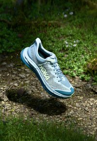 Light blue running shoe with textured upper, white and green accents, cushioned sole, and lacing system, set against a natural background.