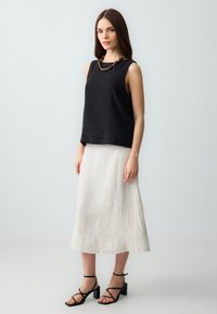 Schwarzes Leinen-Top ohne Ärmel, cremefarbenen Leinen-Midi-Rock und schwarze Sandalen mit Blockabsatz und Riemchen. Texturierte Materialien, lockere Passform, schlichte Linien.