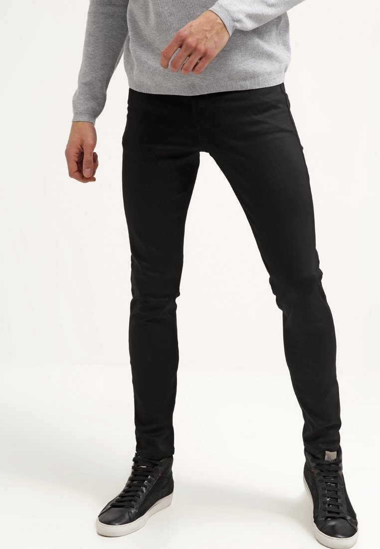 Jean slim noir en denim, avec une texture lisse et un design minimaliste. Associé à des baskets noires et un pull gris.