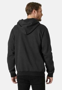 Sudadera negra con capucha ajustable, mangas largas, puños acanalados y dobladillo. El material parece suave y ligeramente texturizado.