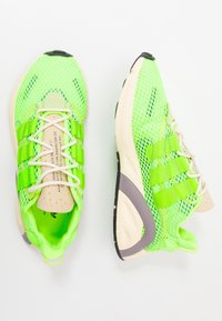 Neon-grüne Netzsportschuhe mit weißen Schnürsenkeln, in Form eines Sportschuhs, mit strukturiertem Obermaterial, gepolstertem Schaft und hellen Sohlenakzenten.