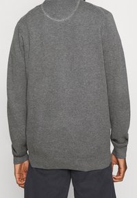 Suéter gris de punto con un patrón texturizado, cuello redondo y puños y dobladillo acanalados. Corte holgado, adecuado para superponer.