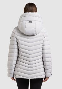 Giacca puffa grigia chiara con design a chevron, collo alto e grande cappuccio. Presenta una texture trapuntata e dettagli in metallo neri.