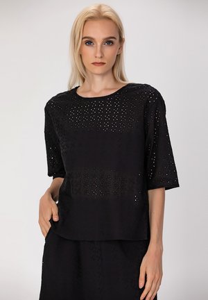 Haut noir avec un design en œillets, manches courtes, encolure ronde, tissu léger, présentant un motif texturé et une coupe décontractée.
