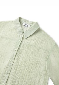 Camisa de color verde claro con cuello, hecha de un tejido texturizado, que presenta pequeñas rayas alternas y un cierre frontal de botones, con botones transparentes y un sutil brillo.