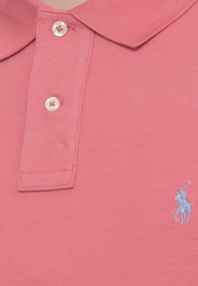 Polo rose texturé avec deux boutons blancs et un petit logo brodé d'un joueur de polo en bas à droite.