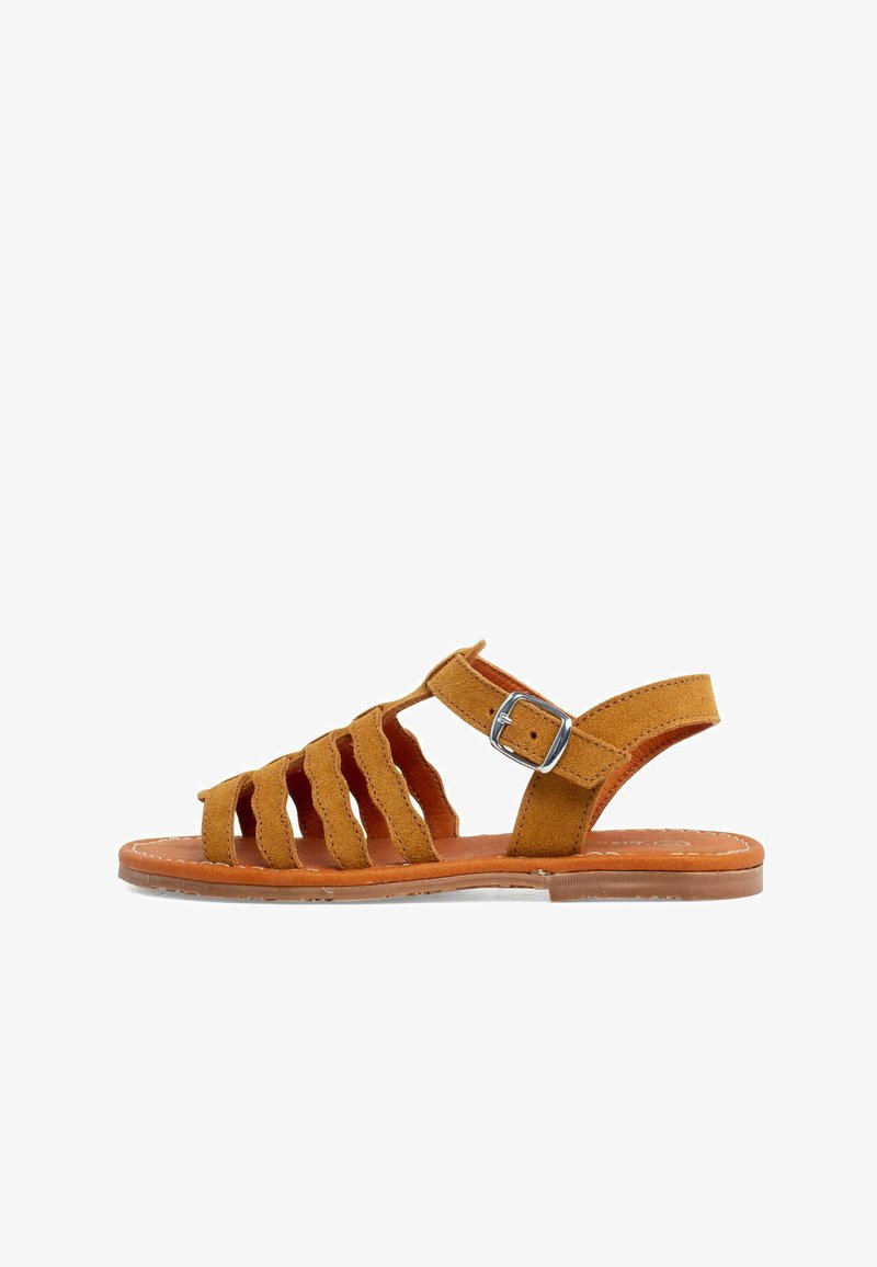 Hnedé nubukové sandále s viacerými vykrajujúcimi detailmi a nastaviteľným remienkom na členku, s plochou podrážkou a kontrastným hnedým prešívaním. Detail s prackou.