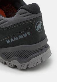 Czarne zamszowe buty trekkingowe z szarymi akcentami, teksturowana gumowa podeszwa oraz logo Mammut; cechują się wzmocnionym zapiętkiem i wyściełanym kołnierzem dla lepszego wsparcia.