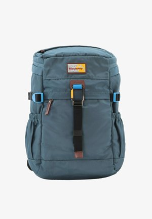 Backpack in dark blue fabric with a logo patch, adjustable buckle, front straps, and side pockets. Smooth texture with a compact design.