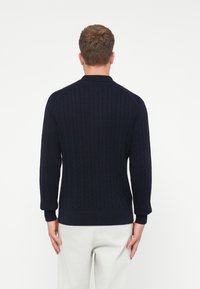 Granatowy sweter z dzianiny z wzorem w warkocz, z prążkowanym kołnierzem i mankietami oraz dopasowanym fasonem w talii. Model jest widoczny z tyłu.