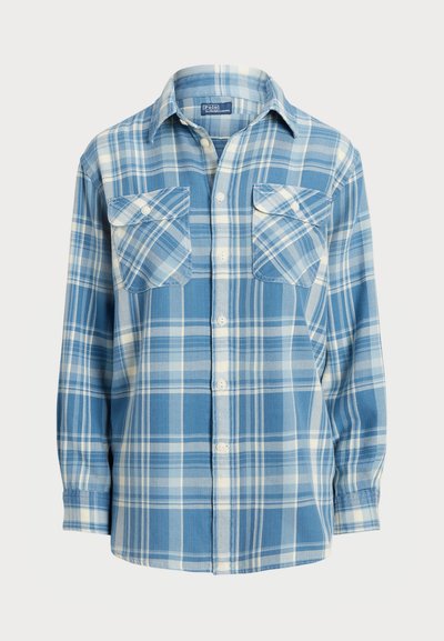 Camicia a quadrati blu con bottoni e maniche lunghe, dotata di due tasche sul petto, con una texture morbida e un motivo a scacchi in diverse sfumature di blu e bianco.
