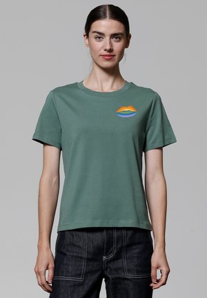 Groene katoenen T-shirt met een ronde hals, korte mouwen en een multikleurige lipgrafiek op het linkerbovenbeen. Zachte textuur en een relaxte pasvorm.