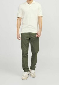 Světle krémové polo tričko s krátkým rukávem a třemi knoflíky, spárované s rovnými kalhotami olivové barvy a béžovými teniskami. Jednoduchý design a střih.