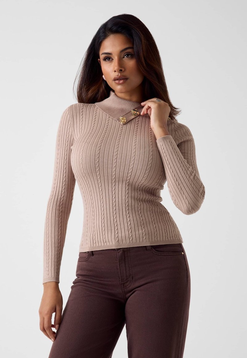 Maglione beige a costine con collo alto e bottoni decorativi dorati sul colletto. Abbinato a pantaloni aderenti marrone scuro.