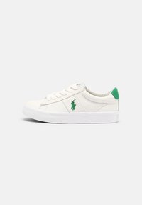 Zapatilla blanca de corte bajo con logotipo y lengüeta verde, cordones blancos y suela de goma, presentada de perfil sobre un fondo sencillo.