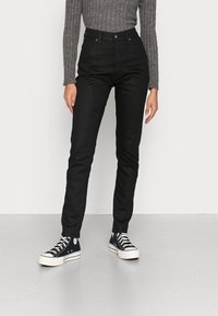 Jeans negros de cintura alta con corte ajustado, fabricados en tela de mezclilla. Combinados con zapatillas altas de color azul oscuro con suelas blancas.