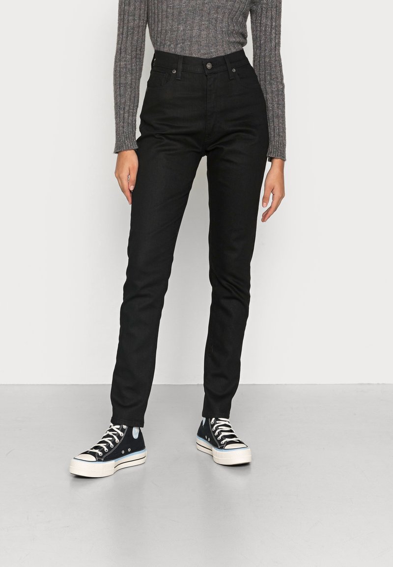 Jeans negros de cintura alta con corte ajustado, fabricados en tela de mezclilla. Combinados con zapatillas altas de color azul oscuro con suelas blancas.