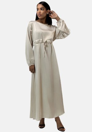 Vestido maxi de satén beige con mangas largas, puños elásticos y cintura ajustable con cordón. Presenta una textura suave y una silueta fluida.