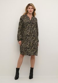 Abito animalier nero e beige con colletto, maniche lunghe e chiusura a bottoni, abbinato a stivaletti neri. 