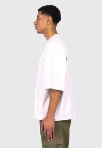 Lightweight white t-shirt with a single chest pocket, short sleeves, and a relaxed fit, paired with olive green cargo pants.