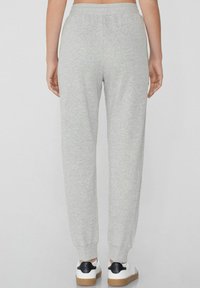 Grijze sweatshirtbroek met een gladde textuur, een elastische tailleband en taps toelopende pijpen. Gecombineerd met witte schoenen met een zwart accent.