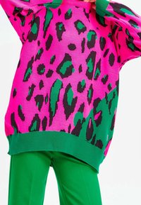 Pull en maille rose vif avec des taches léopard noires et vertes ; poignets et ourlet verts côtelés ; associé à un pantalon vert uni.