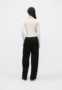 Kremowa bluzka z długim rękawem ozdobiona czarnymi przeszyciami, zestawiona z czarnymi, szerokimi spodniami z wysokim stanem, charakteryzującymi się luźnym krojem i gładką tkaniną.