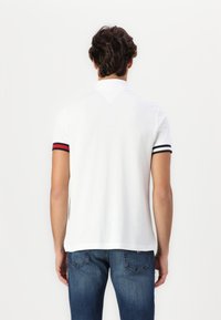 Hvit polo med kort erme som har svarte og røde stripete detaljer. Myk stoff, litt innsnevret design og en klassisk krage.