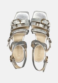 Sandali con tacco argentato e punta quadrata, caratterizzati da più cinturini, dettagli dorati e una finitura metallica liscia. Logo del brand visibile sulla soletta.