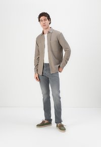 Cămașă albă deschis cu nasturi, cu două buzunare pe piept, purtată peste un tricou alb, asociată cu blugi gri deschis și pantofi din velur verde.
