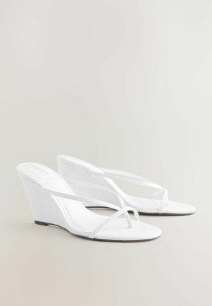Sandali wedge bianchi con fasce sottili per le dita e alla caviglia, design open-toe e suola leggermente appuntita su uno sfondo neutro.