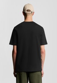 Camiseta negra de manga corta hecha de algodón, con cuello redondo; combinada con pantalones caquis y una gorra de béisbol beige.