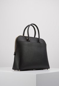 Czarna torebka wykonana z teksturowanego materiału syntetycznego. Posiada zaokrąglone uchwyty, złoty zamek błyskawiczny oraz metalowe nóżki dla stabilności. Projekt jest usztywniony.