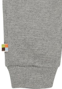 Tessuto di maglia grigia con texture a coste. Presenta un'etichetta colorata con quadrati verdi, arancioni, blu e marroni sul lato.