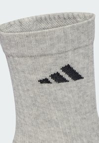 Siva pamučna čarapa s rebrastom teksturom, s crnim Adidas logotipom sa strane. Vrh je malo preklopljen.