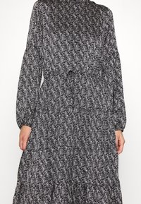 Robe à motifs noir et blanc avec des manches longues, des poignets élastiques, une taille cintrée et un design de jupe à volants. Texture de tissu douce et fluide.