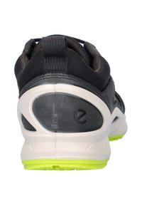 Scarpa sportiva nera con tomaia testurizzata, suola intermedia bianca e suola esterna verde brillante. Presenta un linguetta sul tallone e dettagli del logo.