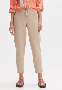Beige, rechte broek van een katoenmix met een elastische tailleband en voorzakken. Draagt een koraalgestreept shirt en bruine sandalen.
