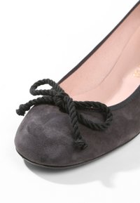 Gros plan sur une ballerine en daim gris foncé avec un nœud en corde noire torsadée sur l'avant arrondi et une doublure intérieure rose clair.