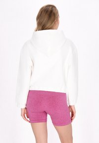Vit kortärmad hoodie med huva, med elastiska ärmslut och nederkant. Matchad med figurnära rosa shorts i ett texturerat, elastiskt material.