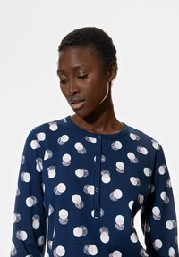 Chemise à manches longues navy avec un motif de formes circulaires blanches et rose pâle accentuées de textures ; col à boutons.