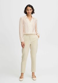 Light pink collared shirt with black polka dots, paired with beige tapered trousers and beige flats. Smooth fabric with a relaxed fit.