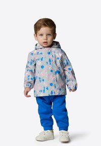 Ljusgrå vattentät jacka med blå djur- och växtmönster, tillsammans med blåa sweatpants och vita slip-on skor.