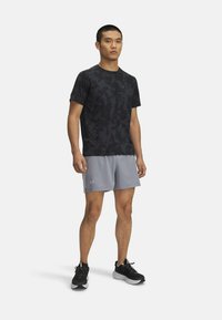 Juodai kamufliažo raštuotas sportinis marškinėliai, derinami su šviesiais pilkais šortais. Šortai turi šoninius tinklo įdėklus ir "Under Armour" logotipą. Juodi bėgimo batai.