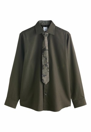 Tumši olīvzaļu garām piedurknēm krekls ar teksturētu rakstu, kombinēts ar pelēku ziedu kaklasaiti. Abiem ir pogu aizdare un kontrastējošs iekšējais apkakle.