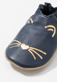 Pantofiu pentru bebeluși din piele bleumarin cu un design în formă de față de pisică, având accente aurii pentru mustăți și un inimioară. Talpa moale din suede pentru confort.