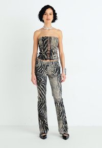 Top sin tirantes y pantalones acampanados en un estampado de cebra en negro y beis atenuados. La tela tiene una textura suave con detalles de cordones en la parte superior.
