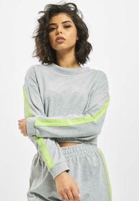 Gray sweatshirt with long sleeves, featuring two green stripes along the arms and an elastic waist. Soft fabric and a relaxed fit.