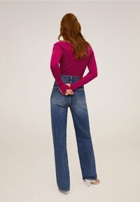 Dopasowana, długosleeve magenta bluzka z prążkowanym wzorem, zestawiona z wysokiej talii, luźnymi niebieskimi dżinsami. Modelka pokazana z tyłu.