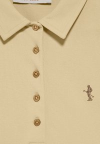 Beżowa koszulka polo z teksturowanej tkaniny, z pięcioma brązowymi guzikami i małym brązowym haftowanym golfistą po lewej stronie.